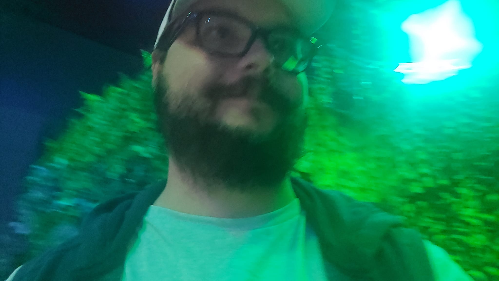 A blury photo of a man with a ball cap and bushy facial hair standing in green light